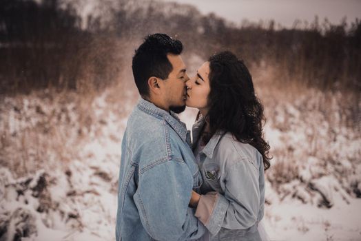 Mexican Hispanic man in denim jacket oversized and woman are kissing hugging laughing. groom and bride wedding love couple in winter in snow. fashionable stylish party wedding wear 2021