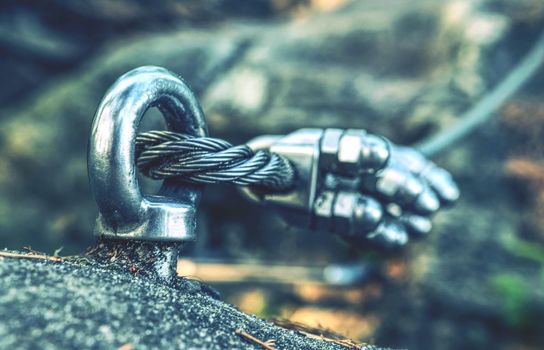 Climbing carabiner attached to cliff rock.  Detail of via ferrata steel cable attached to stainless iron rod on mountain top Shallow depth of field.