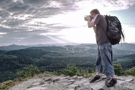 Man holding camera at eyes on mountain and watching sunset.