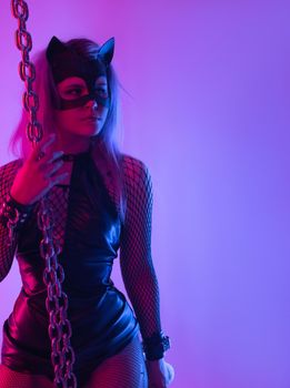 Sexy girl in latex dress bdsm mistress and cat mask in neon light with chains for sex games