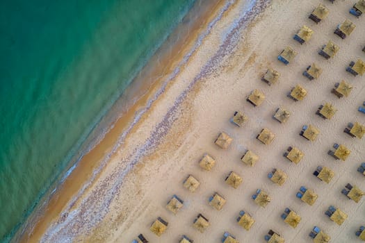 Aerial view of an amazing beach with wooden umbrellas, and calm sea.