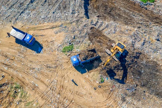 Aerial top view of excavator and dump trucks working at the construction site