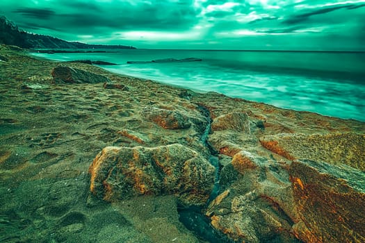 Creative view of cloudy sunrise with motion blur sea and rocks on the beach