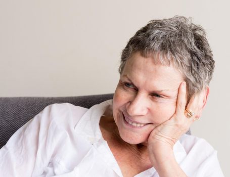Older woman with short grey hair smiling with hand on head in relaxed position (selective focus)