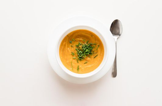 High angle view of roasted root vegetable soup with sprinkled chives in white bowl on table with spoon