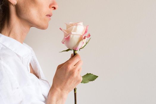 Profile view of middle aged woman holding single pink and cream rose (cropped)