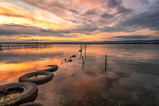 Beautiful sunset on the lake with fishing net in water and old tires 