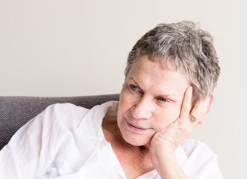 Older woman with short grey hair and white shirt with hand on head in relaxed position (selective focus)