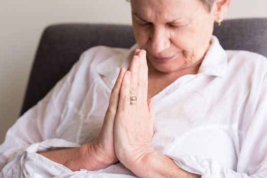 Older woman in white shirt seated with hands clasped in prayer (selective focus and cropped)