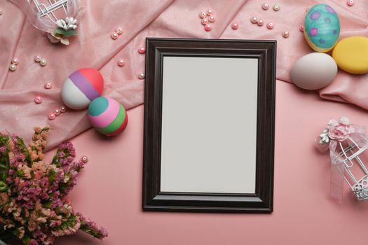 Empty picture frame with painted Easter eggs and spring flowers on pink background. Happy Easter concept.