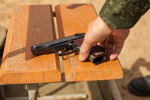 A military man in uniform. A man's hand takes a gun