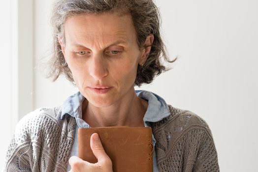 Head and shoulders view of middle aged woman with grey hair frowning and holding book (selective focus)