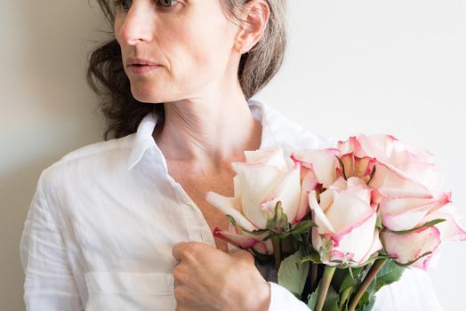 Middle aged woman in white shirt holding bouquet of pink and cream roses (cropped and selective focus)