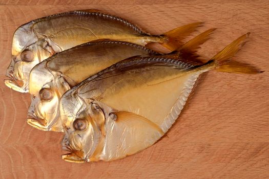 Three smoked vomer fish lie on a wooden board