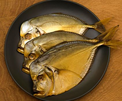 Three smoked vomer fish, lie on a black plate on a wooden board