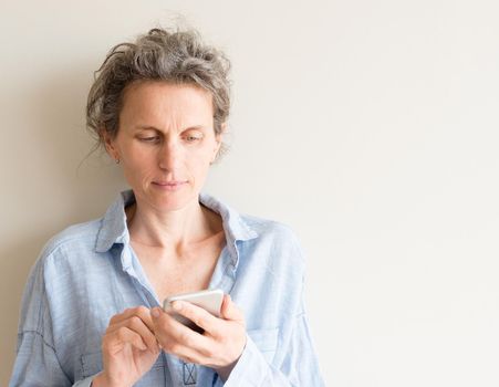 Middle aged woman with grey hair and blue shirt using smart phone