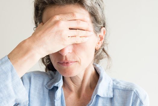 Close up of middle aged woman with hand covering eyes