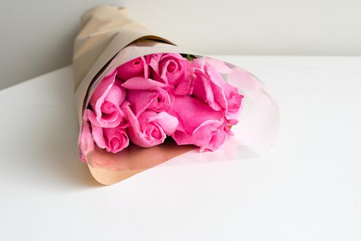 Close up of pink roses wrapped in brown paper and cellophane on white table (selective focus)