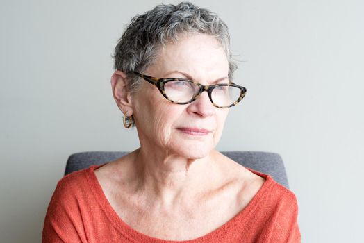 Older woman in orange top with glasses looking thoughtful against neutral background