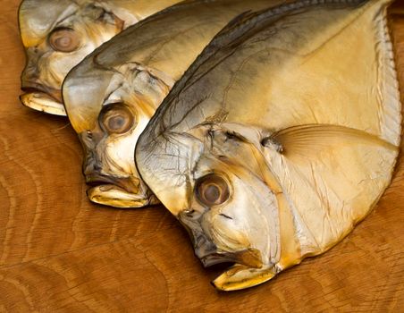 Three smoked vomer fish lie on a wooden board