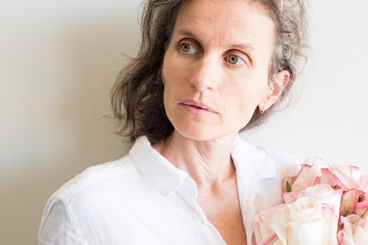 Middle aged woman with grey hair and white shirt holding pink and cream roses (cropped)