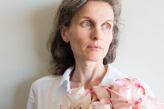 Middle aged woman with grey hair and white shirt holding roses and looking thoughtful