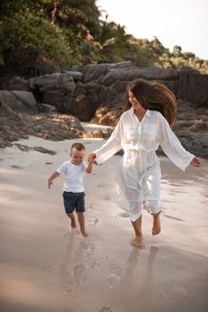Happy smile european family have rest and run on white sand beach. Father, long black chestnut hair mother, blond baby boy. white cotton clothes. boho dress. t-shorts.Thailand. Aquamarine crystal sea