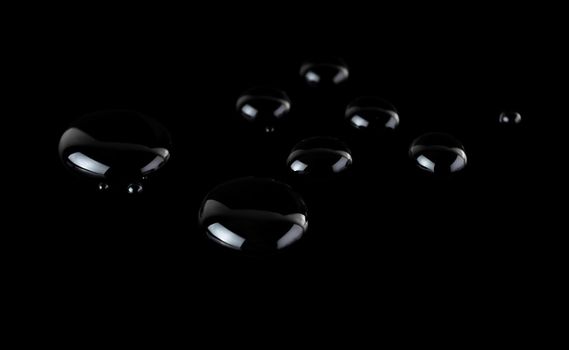 drops of liquid on a black glossy background arranged in a chaotic manner