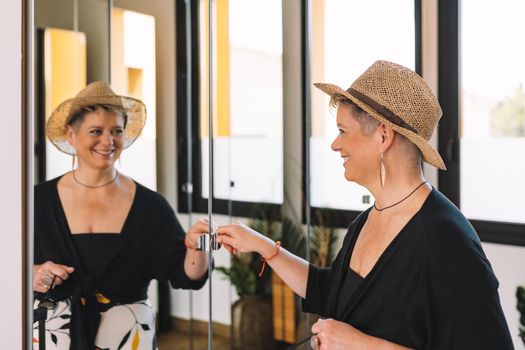 mature woman traveller, looking at herself in the mirror as she dresses to go for a walk along the coast on her summer holiday. bedroom, natural light, dressing room with mirrors.