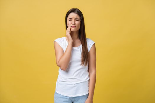 young woman has a toothache, studio photo isolated on a yellow background.