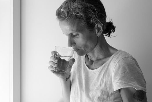 Profile of middle aged woman holding glass and looking pensive - addition concept (black and white)
