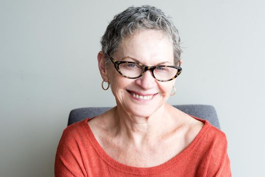 Head and shoulders view of older woman in orange top with glasses smiling