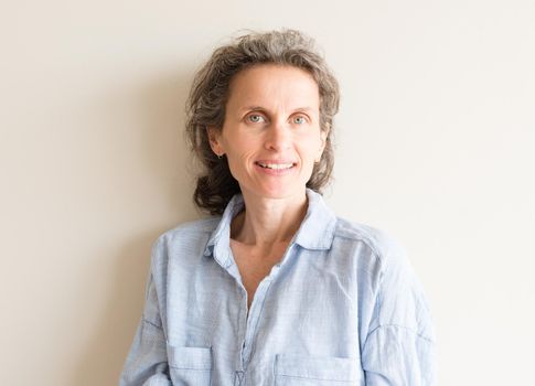 Natural looking middle aged woman with grey hair and blue shirt smiling