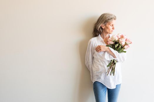 Half length view of middle aged woman with grey hair and white shirt holding pink and cream roses