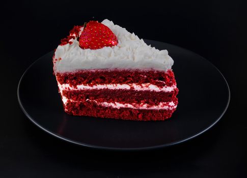 Piece of cake covered with protein cream and strawberries on a black plate and black background