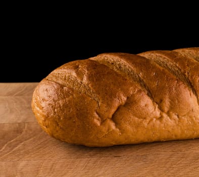 part of a loaf of bread, close-up, on a wooden board on a black background