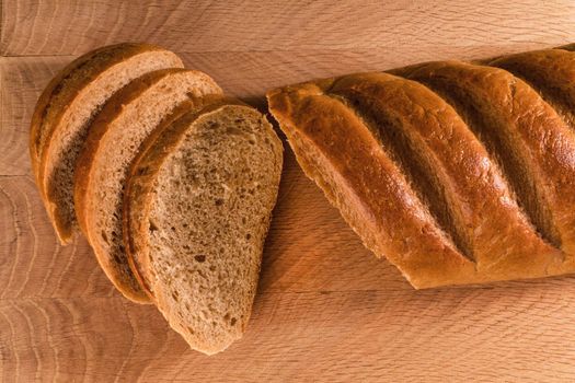 A loaf of bread and slices cut from it laid, on a wooden board, view from the top