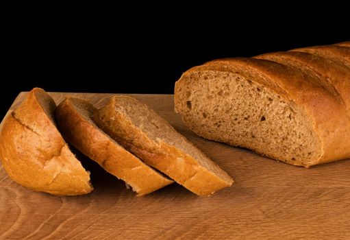 Ruddy loaf of bread and slices cut from it, on a wooden board, on a black background