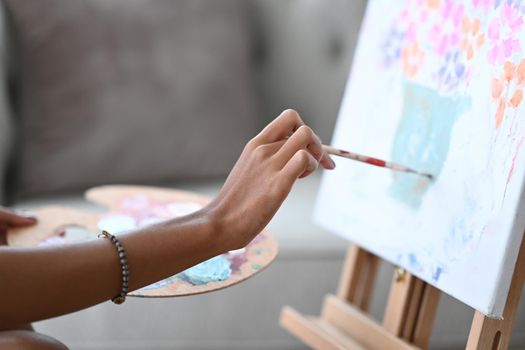 Cropped shot young woman painting picture on canvas with oil paints.