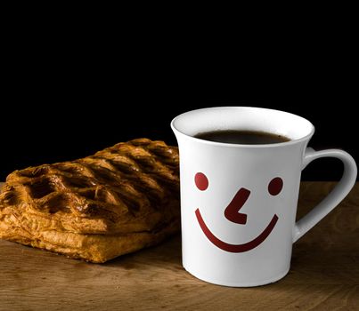 cup with tea and bun on wood board, on black background