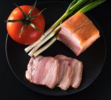 Food, Sliced bacon, tomato green onion, on a black plate, on a black background