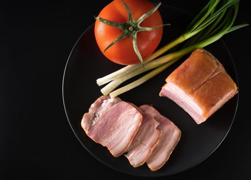 Food, Sliced bacon, tomato green onion, on a black plate, on a black background