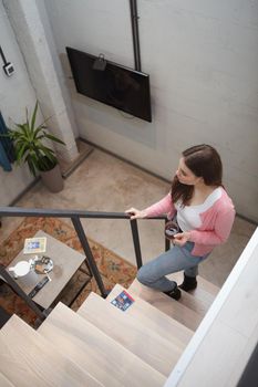 Vertical top view shot of a woman walking up the stairs at her hotel room, carrying cup of tea