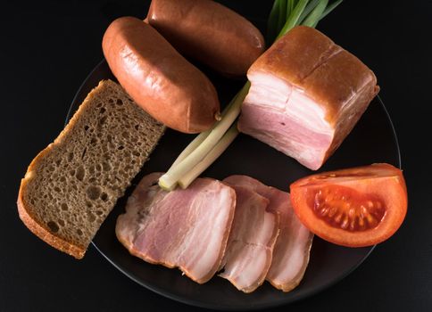 Food, lard green onions, tomato, black bread, sausages, on a black plate on a black background