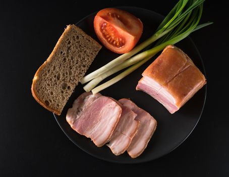 Food, lard, green onions, tomato, black bread, on a black plate, on a black background