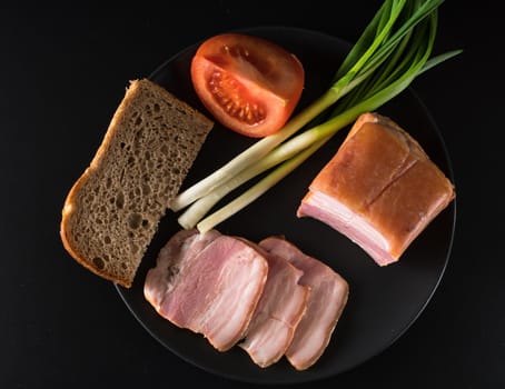 Food, lard, green onions, tomato, black bread, on a black plate, on a black background