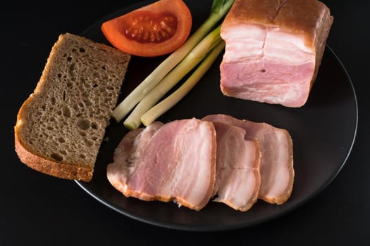 Food, lard, green onions, tomato, black bread, on a black plate, on a black background