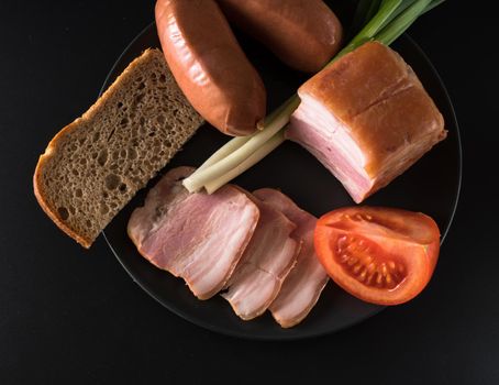 Food, lard green onions, tomato, black bread, sausages, on a black plate on a black background