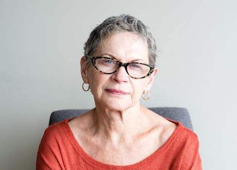 Portrait of older woman in orange top with glasses against neutral background