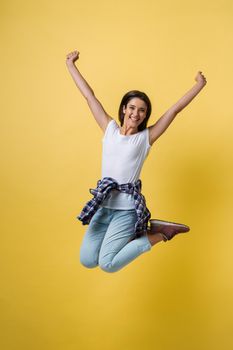 Full-length portrait of carefree girl in white shirt and jean jumping on yellow background